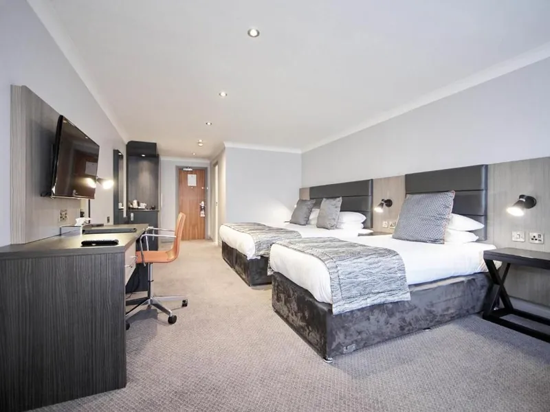 Modern twin hotel room with two beds, a desk and wall-mounted television