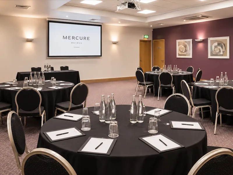 Clinton conference room at Mercure Hotels set with round tables, chairs, water bottles and presentation screen.