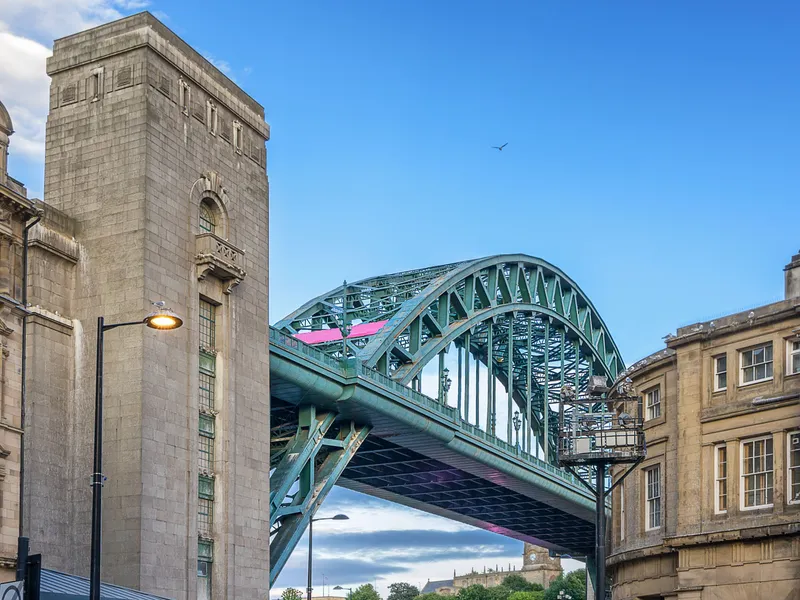 Green steel arch of the Tyne Bridge spanning a street between stone buildings in Newcastle upon Tyne