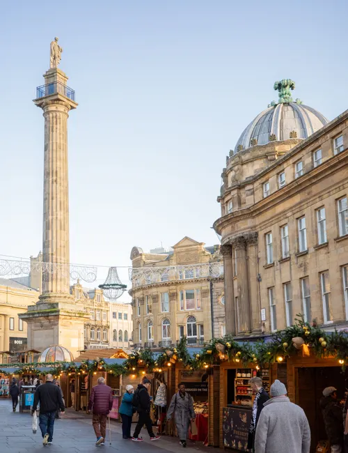 Shoppers walk past decorated Christmas market stalls beneath Grey’s Monument in Newcastle upon Tyne.