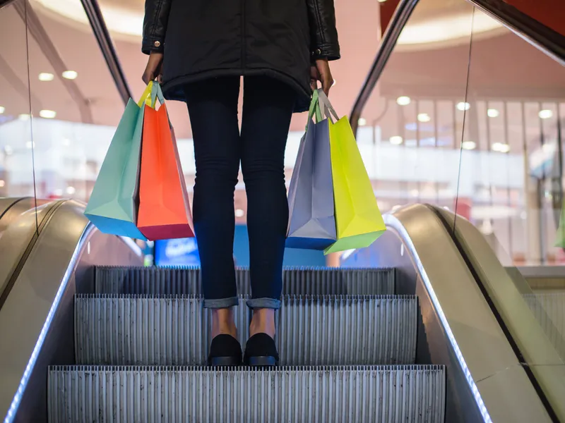 Shopper carrying colourful bags on an escalator in a shopping centre