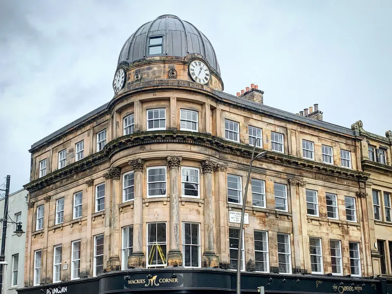 Historic stone corner building at Mackies Corner with a domed clock tower and black shopfronts