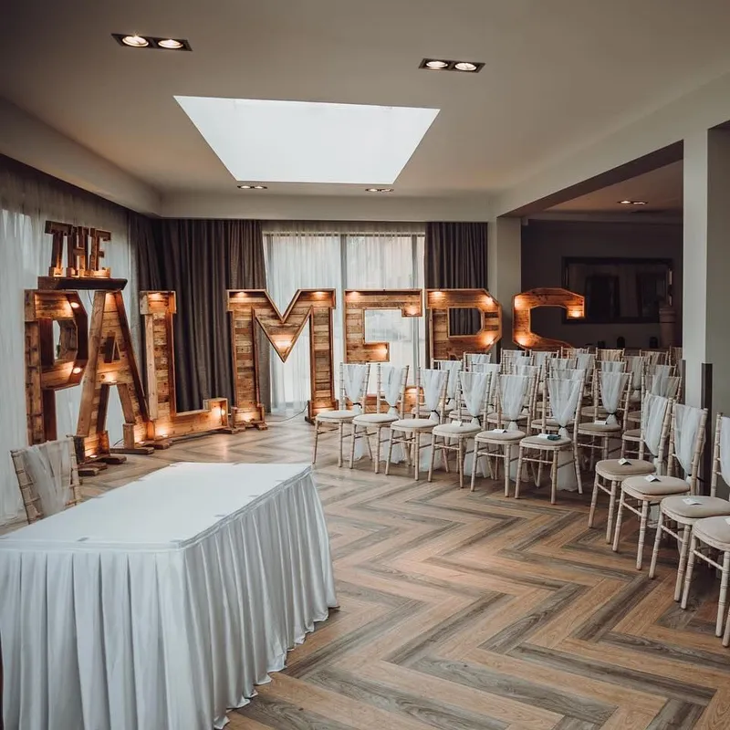 Indoor wedding ceremony venue with rows of decorated chairs and illuminated wooden letters spelling FALMES
