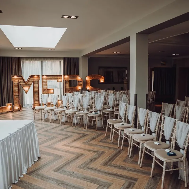 Indoor wedding ceremony venue with rows of decorated chairs and illuminated wooden letters spelling FALMES