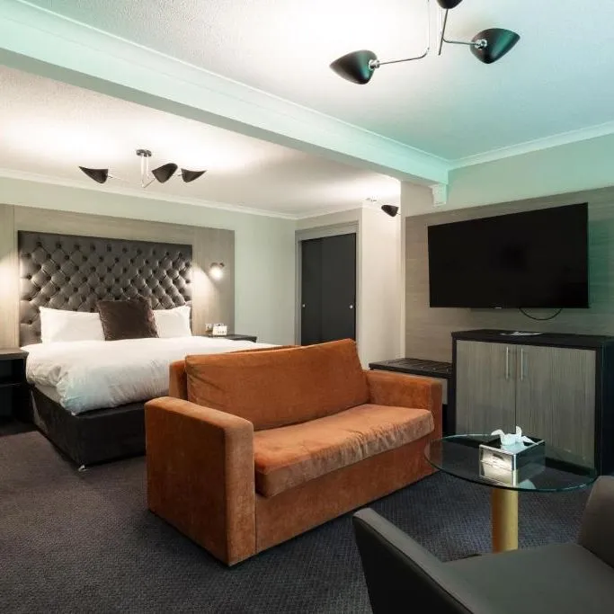 Modern hotel suite with a double bed, orange sofa, armchairs and wall-mounted television