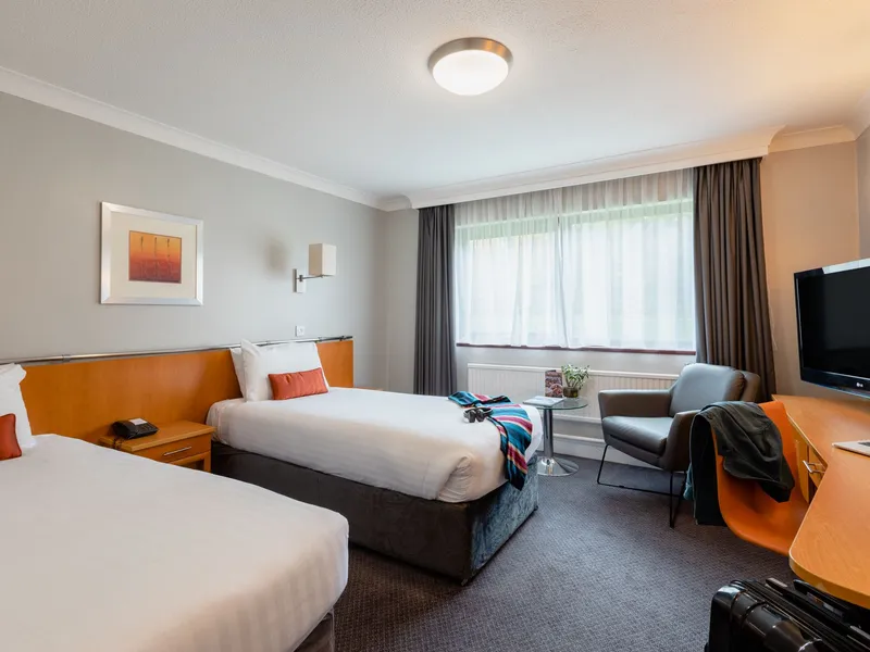 Modern hotel twin room with two beds, desk, television and armchair