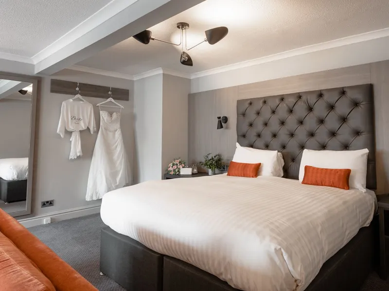 Elegant bridal suite with a tufted bed, orange sofa and wedding dress hanging on the wall