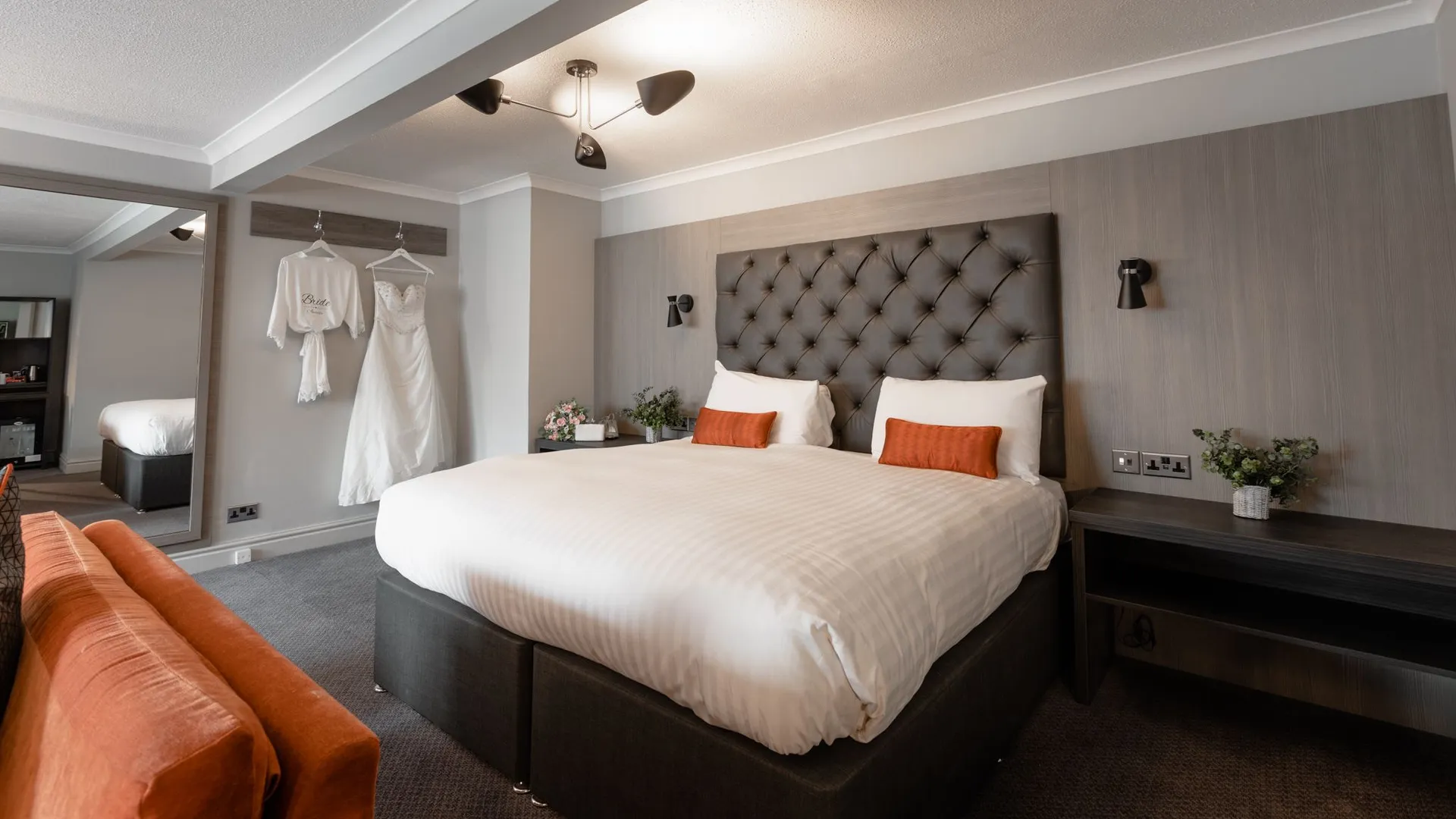 Elegant bridal suite with a tufted bed, orange sofa and wedding dress hanging on the wall