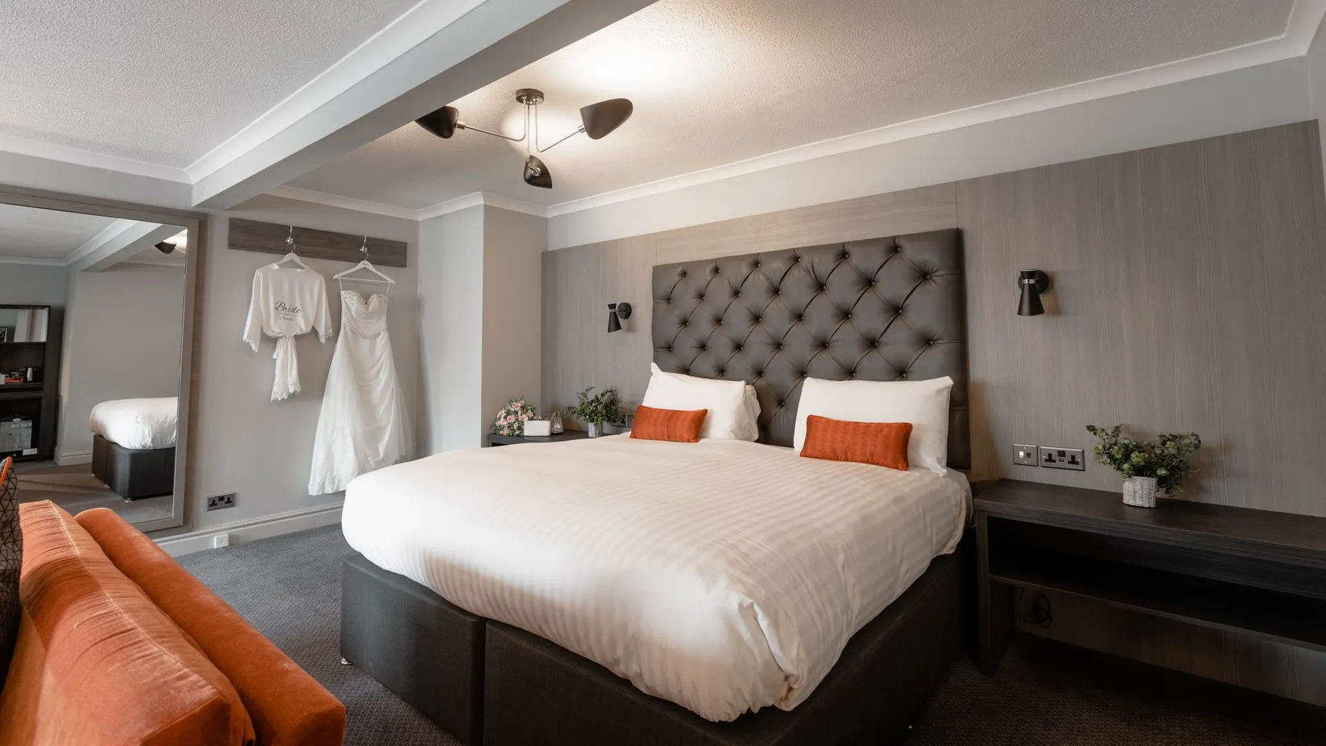 Elegant bridal suite with a tufted bed, orange sofa and wedding dress hanging on the wall