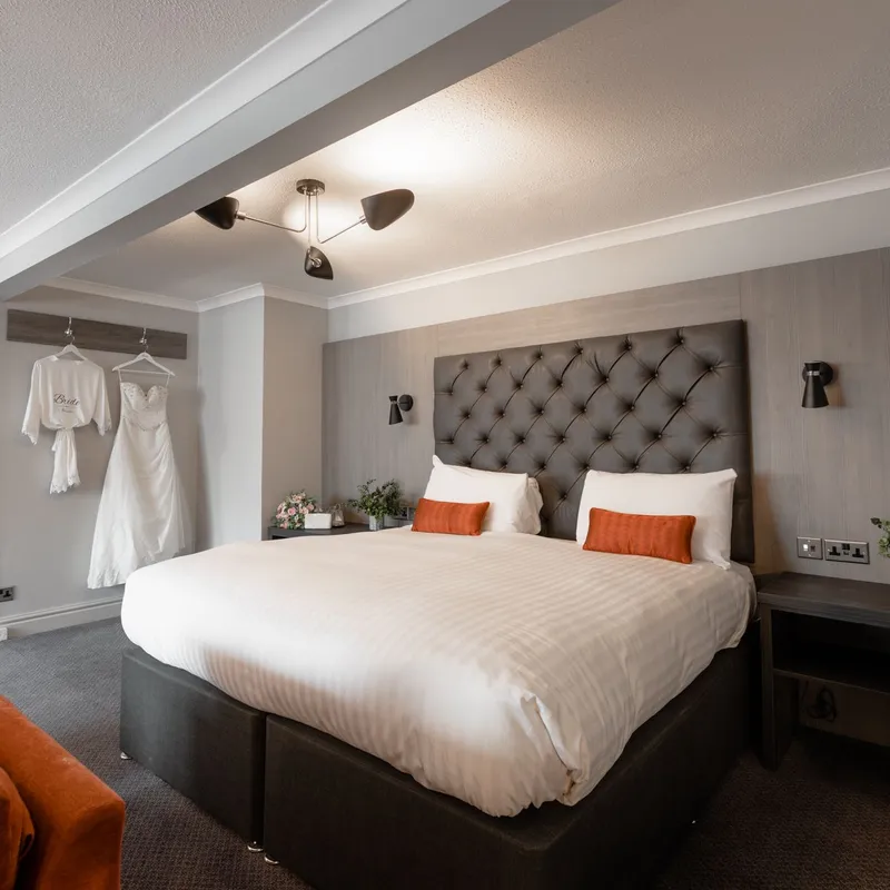 Elegant bridal suite with a tufted bed, orange sofa and wedding dress hanging on the wall