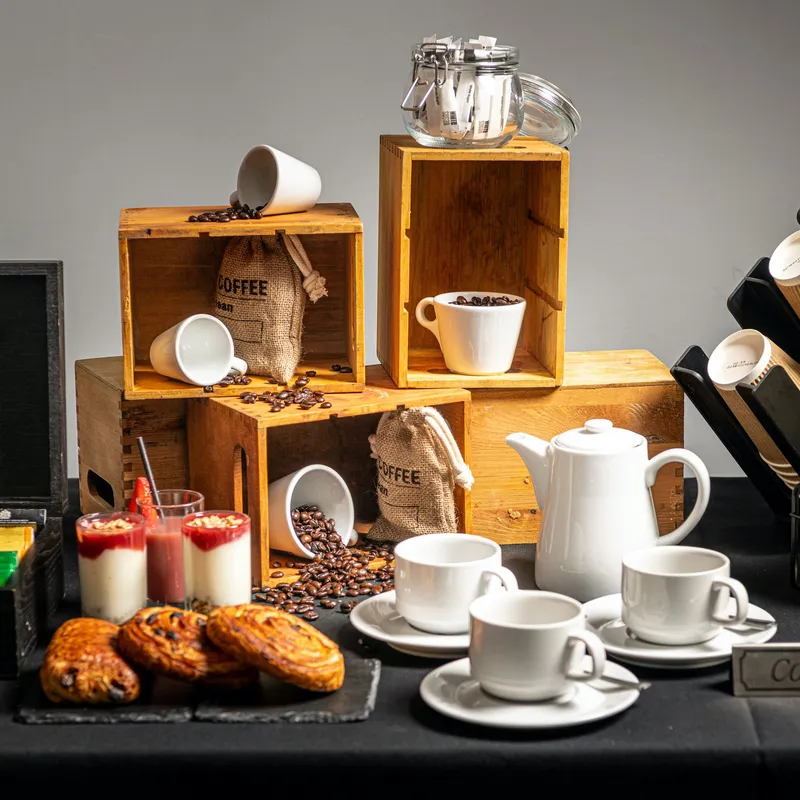 Coffee station display with cups, coffee beans, pastries, syrup bottles and a white teapot.