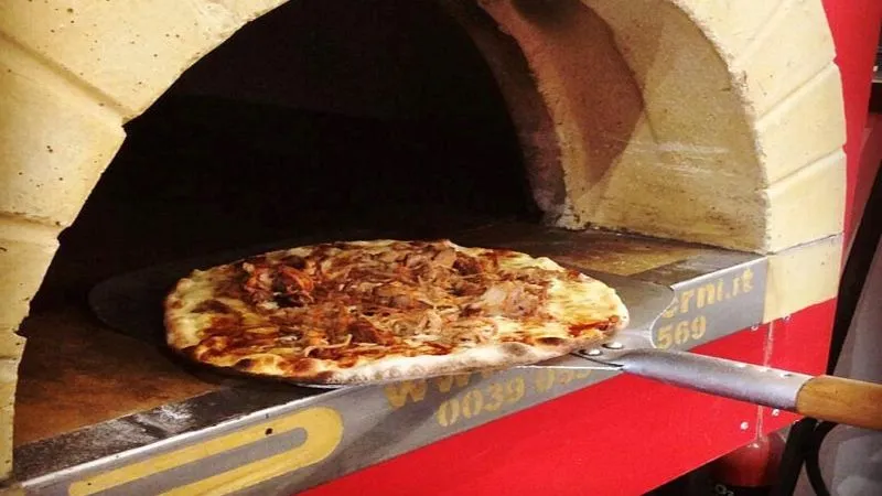 Freshly baked pizza on a peel at the entrance of a wood-fired oven