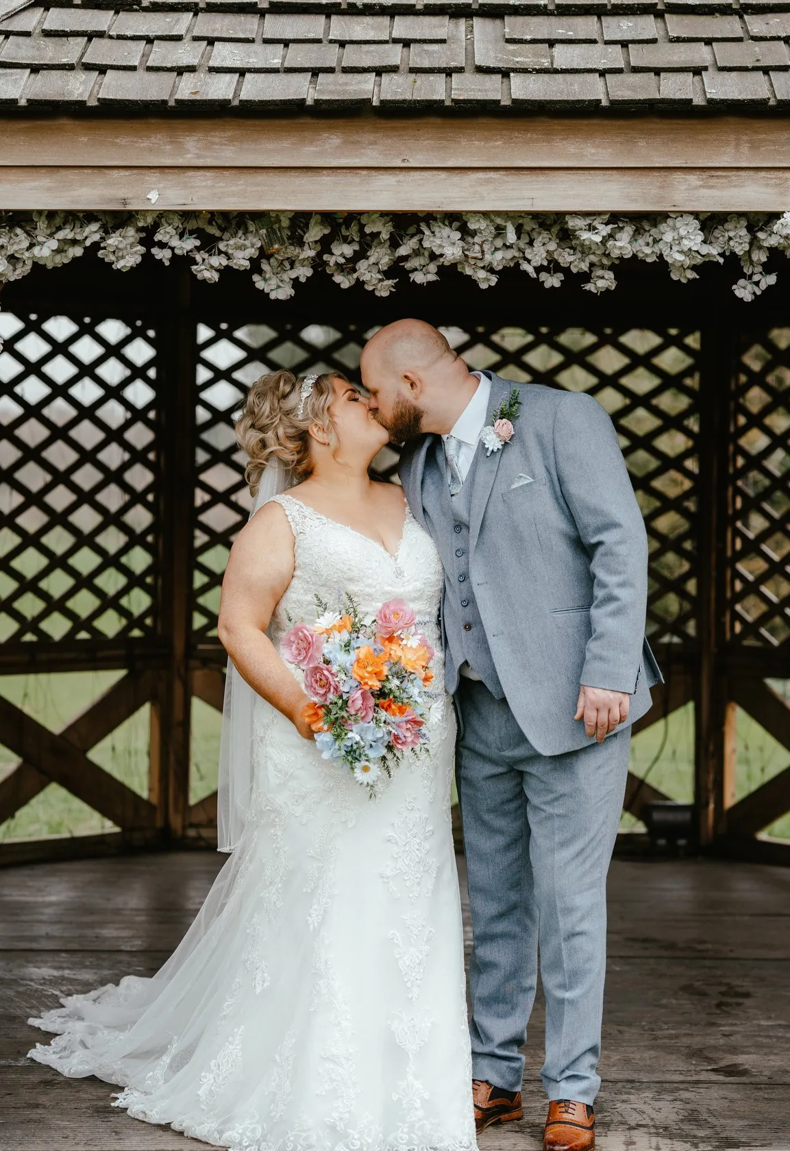 Bride and groom kissing beneath floral decorations at a wooden gazebo