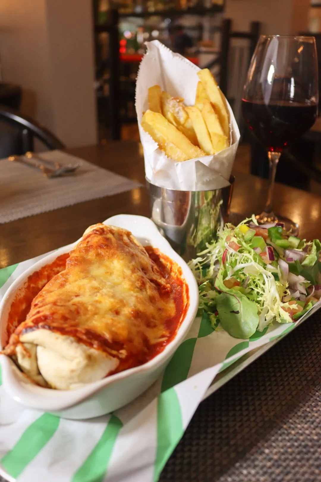 Cheese-topped baked pasta in tomato sauce served with chips, salad and a glass of red wine.
