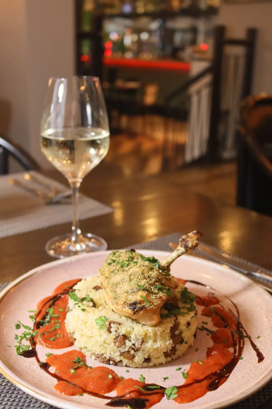 Roasted chicken leg served on couscous with tomato sauce, herbs and a glass of white wine