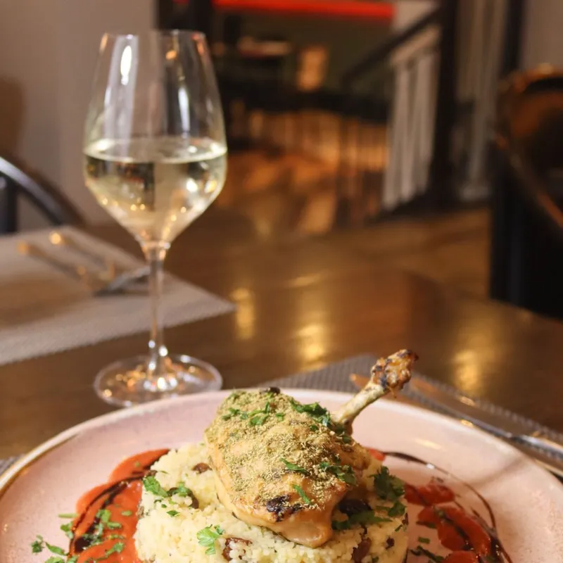 Roasted chicken leg served on couscous with tomato sauce, herbs and a glass of white wine