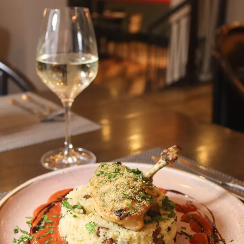 Roasted chicken leg served on couscous with tomato sauce, herbs and a glass of white wine