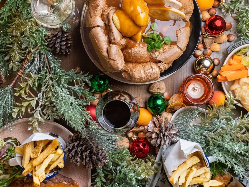 Festive overhead spread featuring a roast dinner in a Yorkshire pudding, steak and chips, fried seafood, Christmas greenery and baubles.