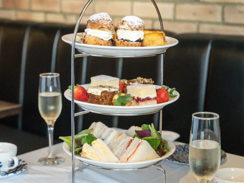 Three-tier afternoon tea stand with sandwiches, cakes and scones beside champagne glasses on a restaurant table.