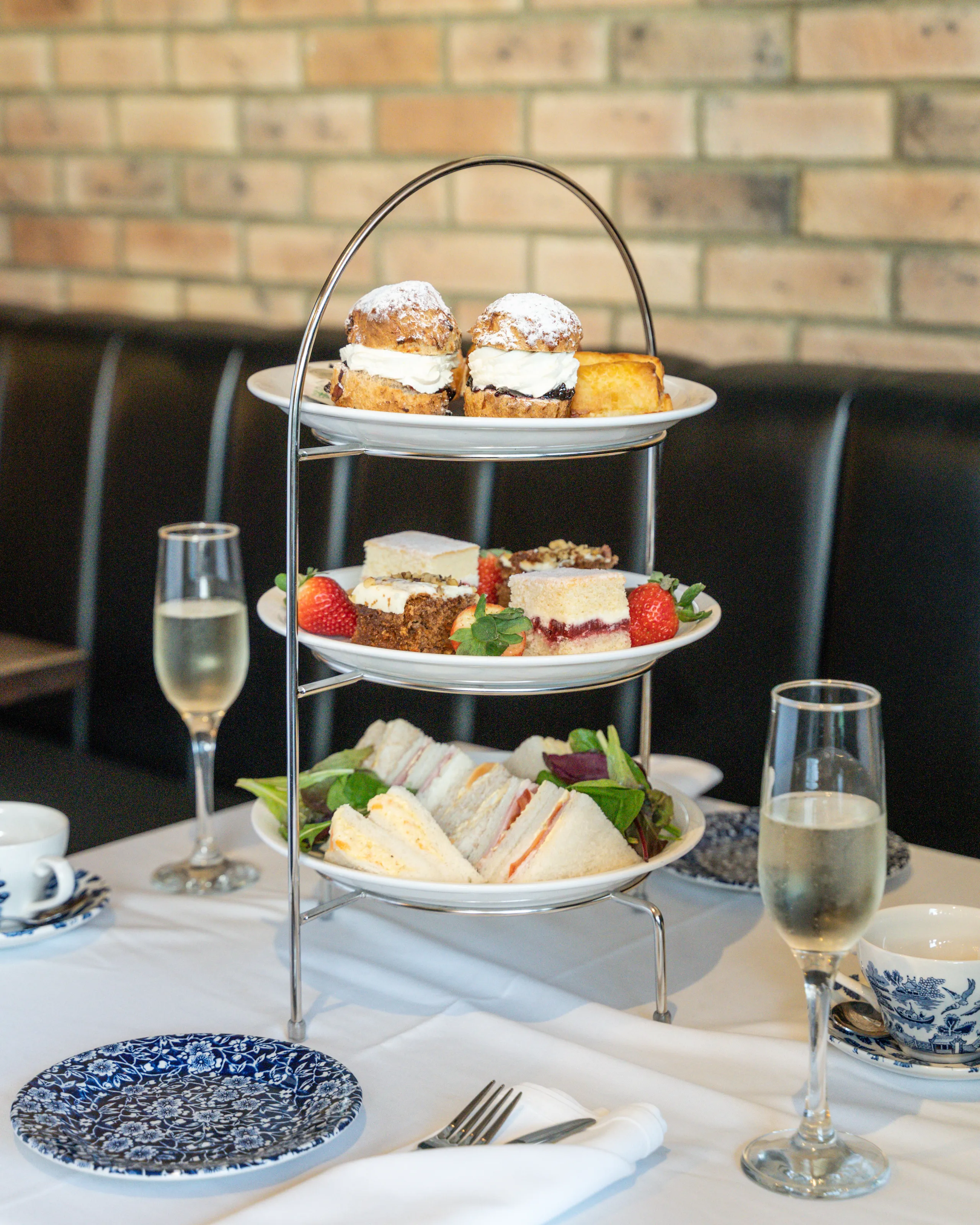 Three-tier afternoon tea stand with sandwiches, cakes and scones beside champagne glasses on a restaurant table.