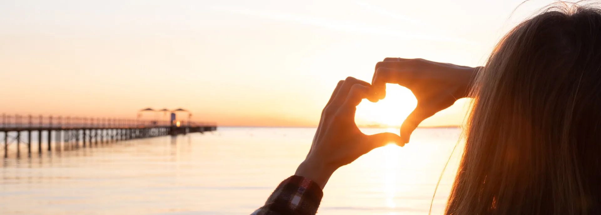 Woman with hands in heart position watching the sunset