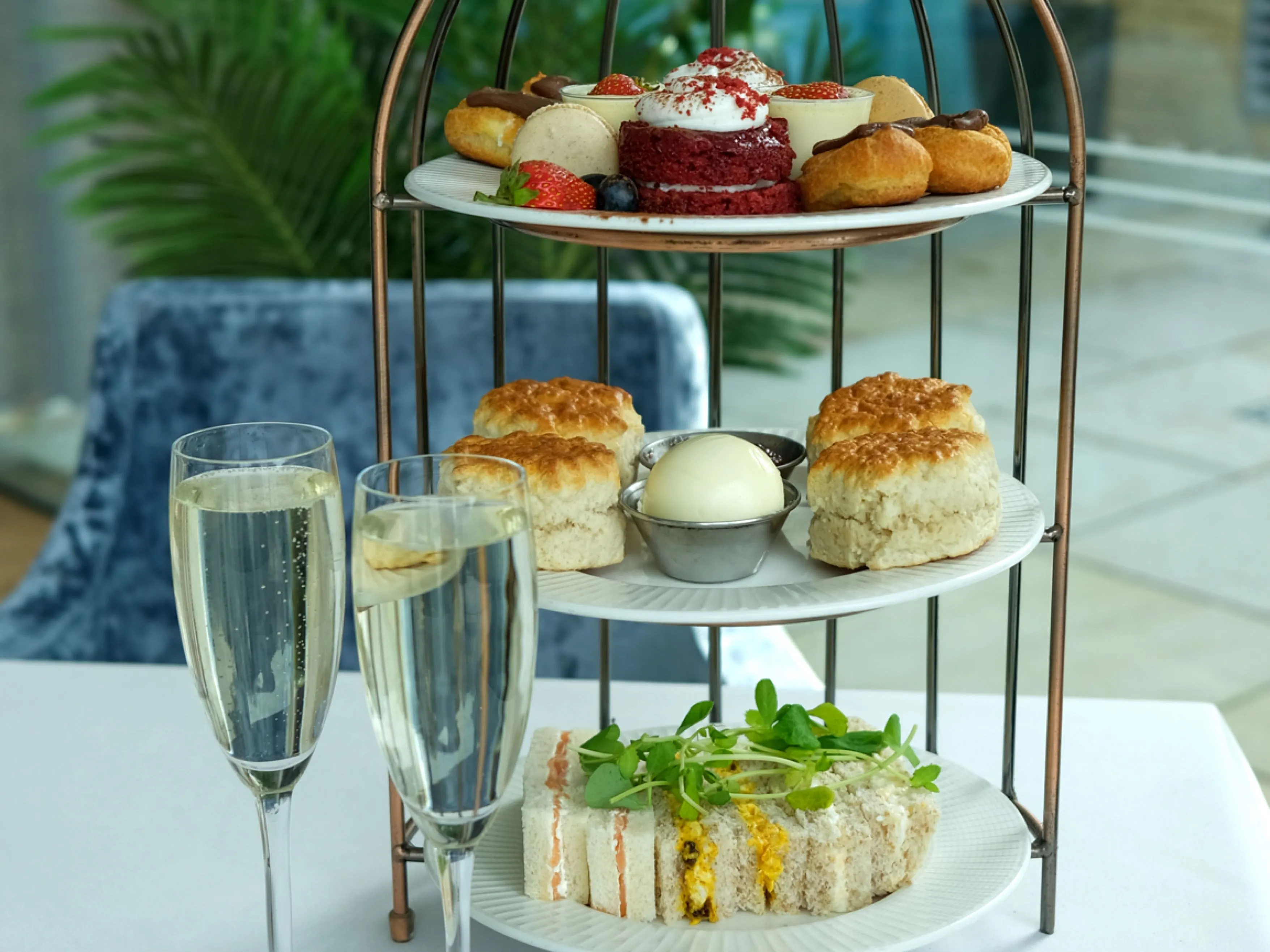 Afternoon tea set with sandwiches, scones, pastries, and two glasses of champagne on a white tablecloth.