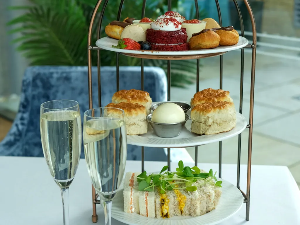 Afternoon tea set with sandwiches, scones, pastries, and two glasses of champagne on a white tablecloth.