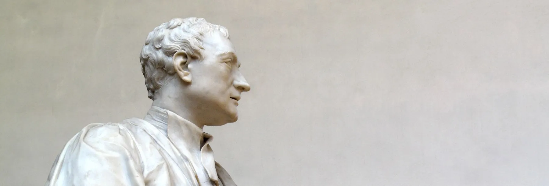Marble statue of Sir Isaac Newton in academic robes, holding a book, shown in profile against a plain background.
