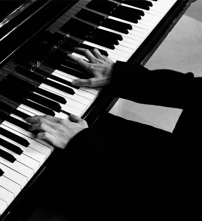 Close-up in black and white of a person playing a C. Bechstein piano, with both hands on the keys and wearing dark sleeves.