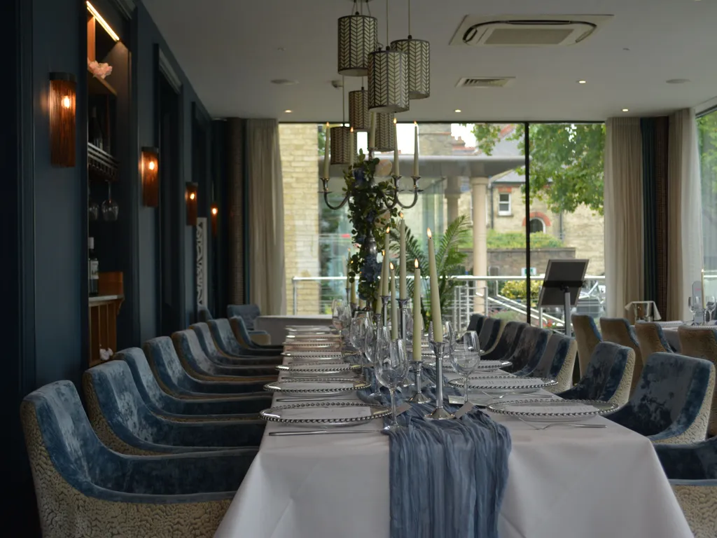 Elegant dining table set for a formal event in a stylish restaurant with velvet chairs and candles.