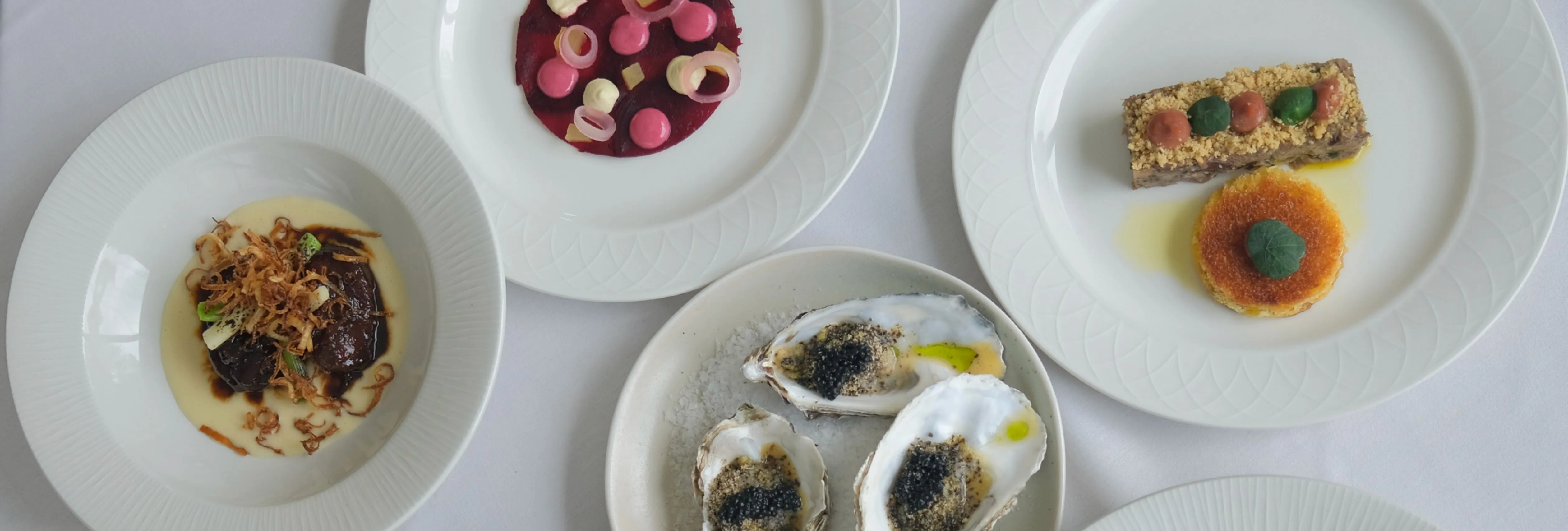 An assortment of gourmet dishes elegantly arranged on white plates atop a white tablecloth.
