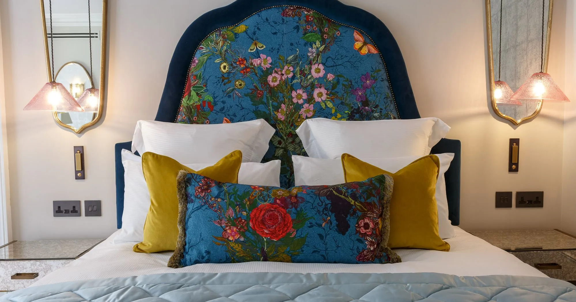Feature bedroom Delphinium's blue floral headboard, colourful pillows, and modern bedside lighting.