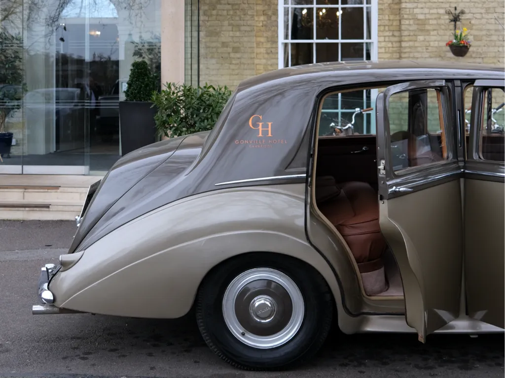The Gonville Bentley parked in front of the Gonville Hotel entrance with an open rear door.