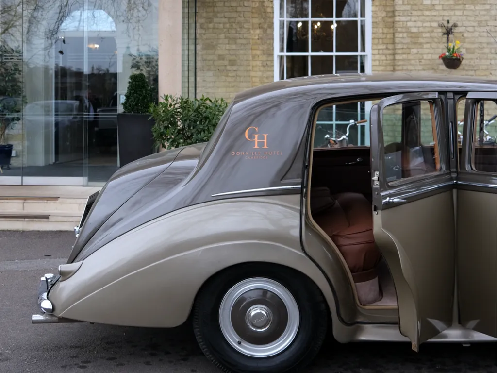 The Gonville Bentley parked in front of the Gonville Hotel entrance with an open rear door.