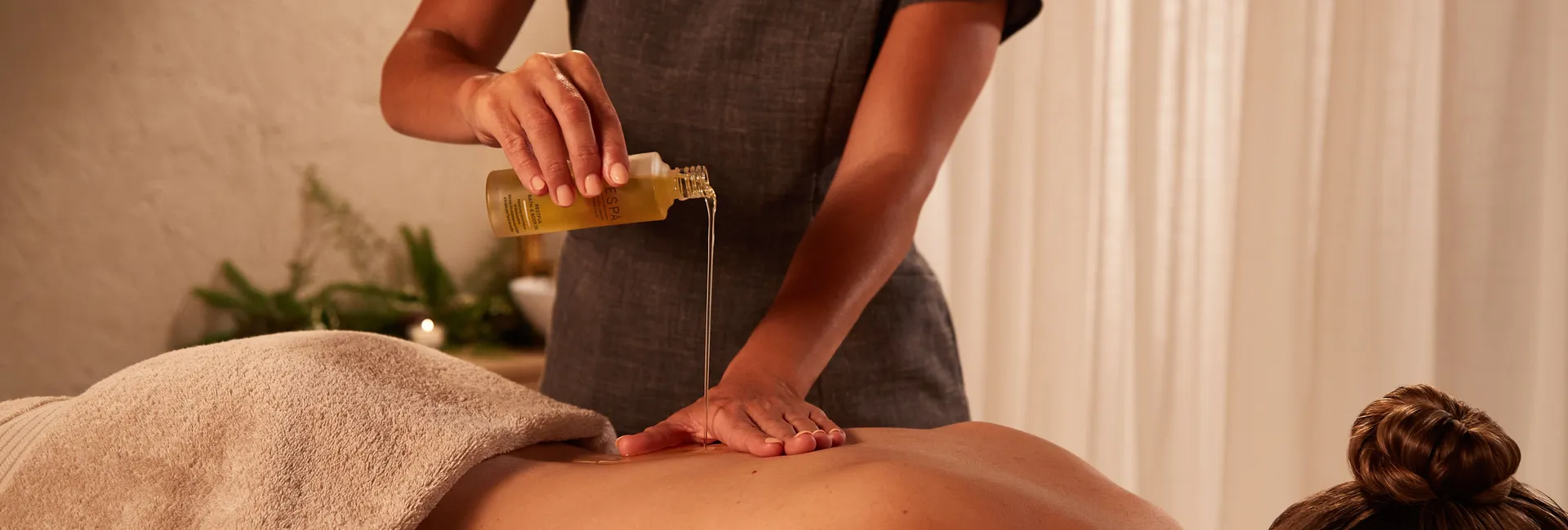 A spa therapist pours massage oil onto a client's back during a treatment.