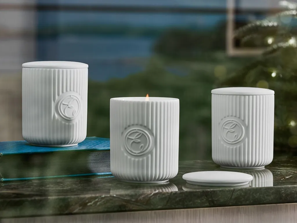 Three white ribbed ceramic candles, one lit, on a marble surface with a scenic background.