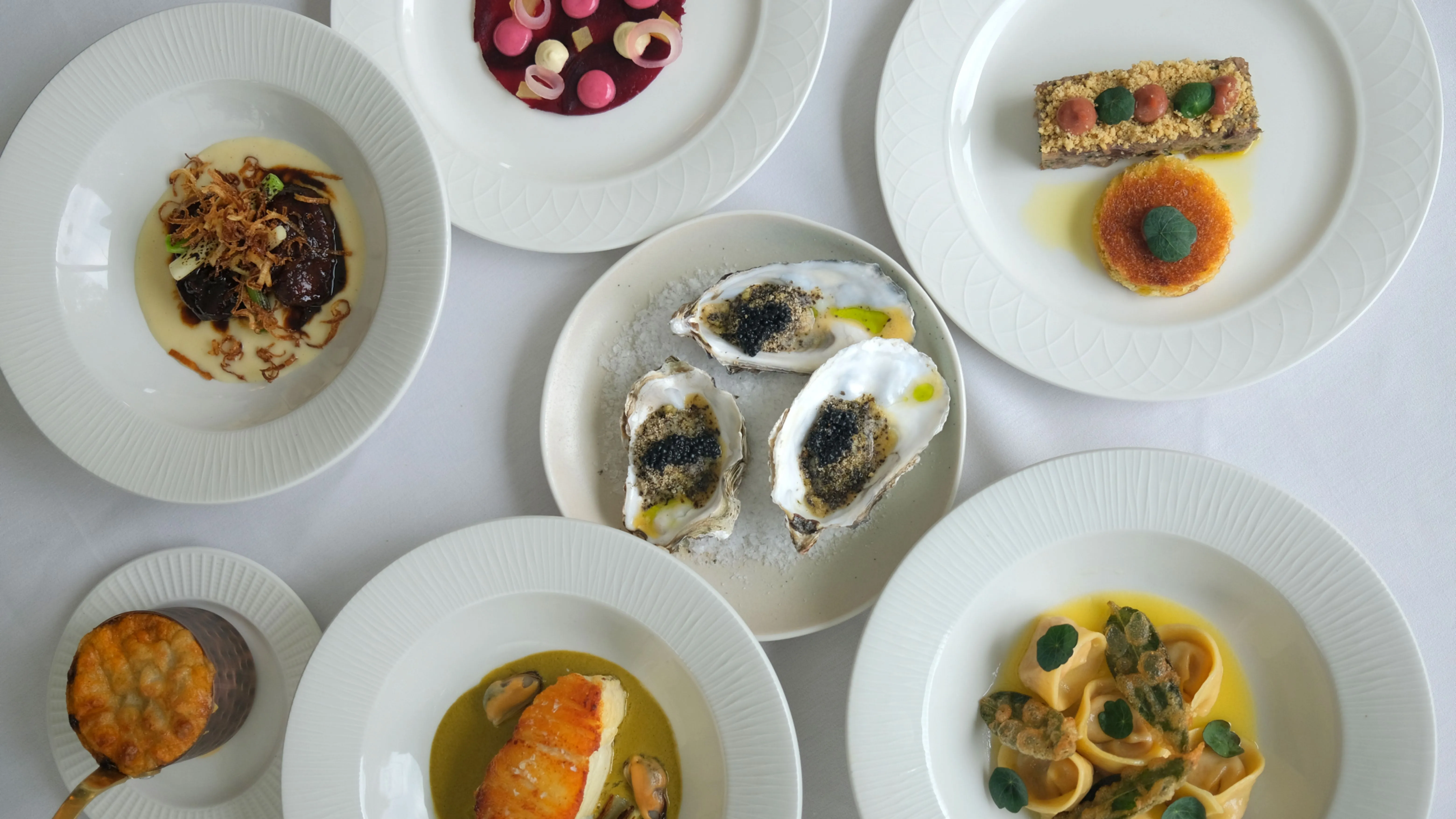 An assortment of six elegant small plates, including oysters, pasta, and seafood, artfully presented at The Gonville Kitchen in Cambridge.