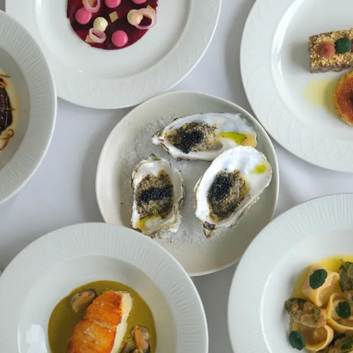 An assortment of six elegant small plates, including oysters, pasta, and seafood, artfully presented at The Gonville Kitchen in Cambridge.
