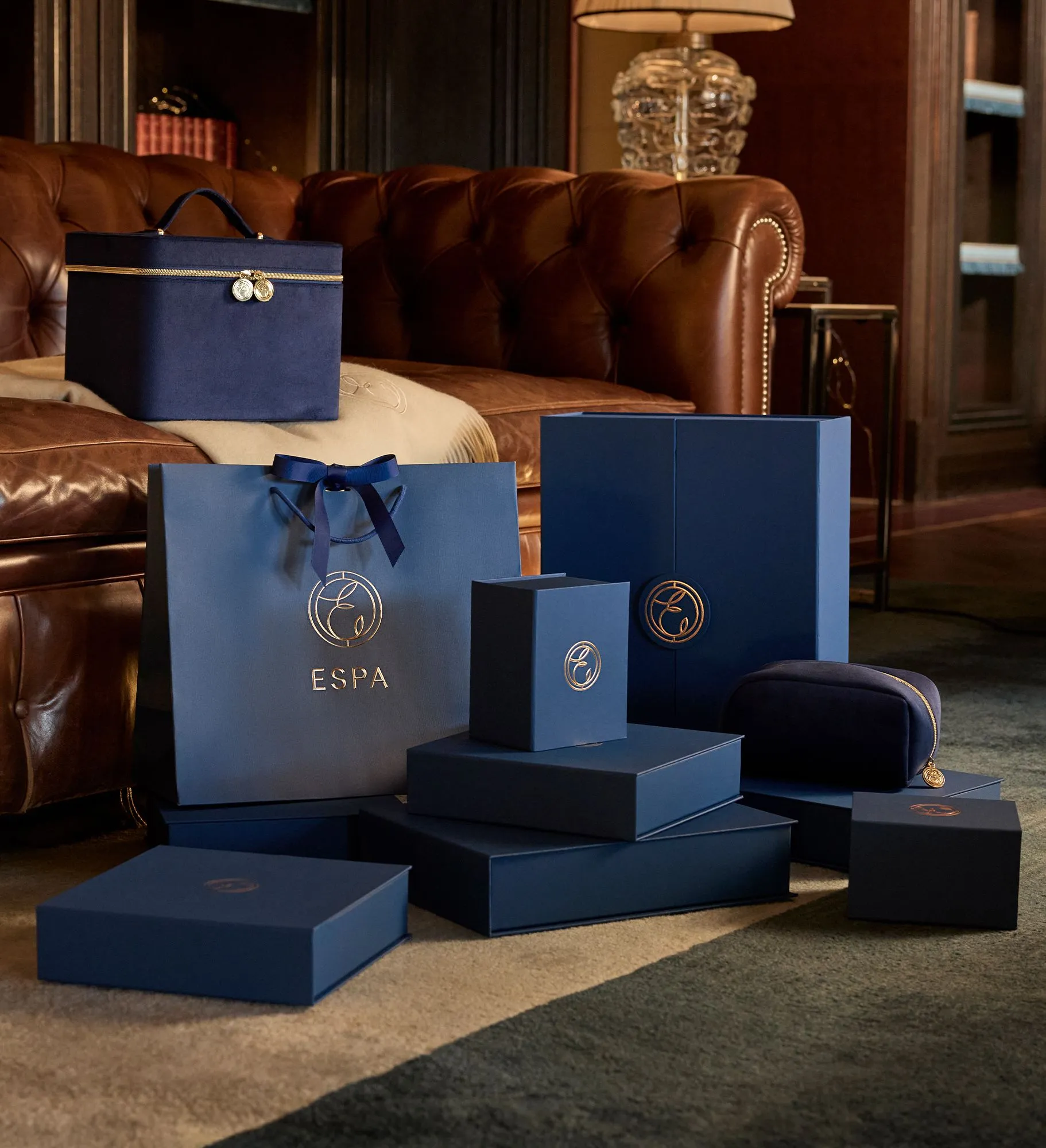 Luxury ESPA gift boxes and bags in dark blue arranged in front of a brown leather sofa.
