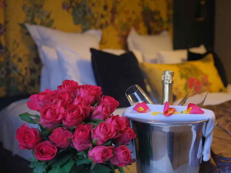 Bouquet of red roses and a champagne bottle in an ice bucket with glasses on a bed in a romantic hotel room