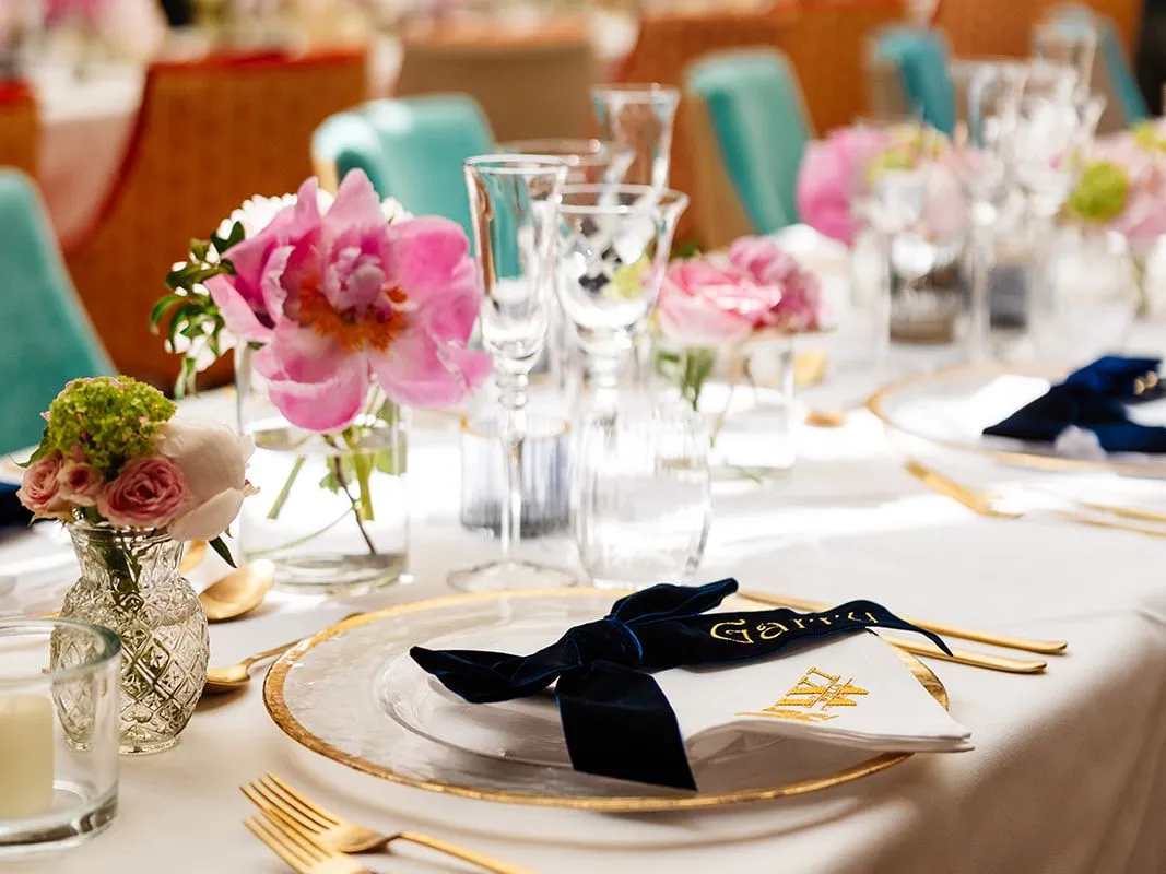Elegant table setting with pink flowers, glassware, gold cutlery, and personalized napkin at a formal event or wedding reception.