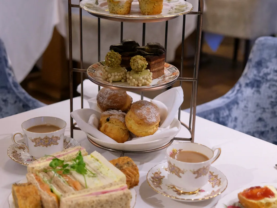 Afternoon tea stand with cakes, scones, sandwiches and two cups of tea on a white table.
