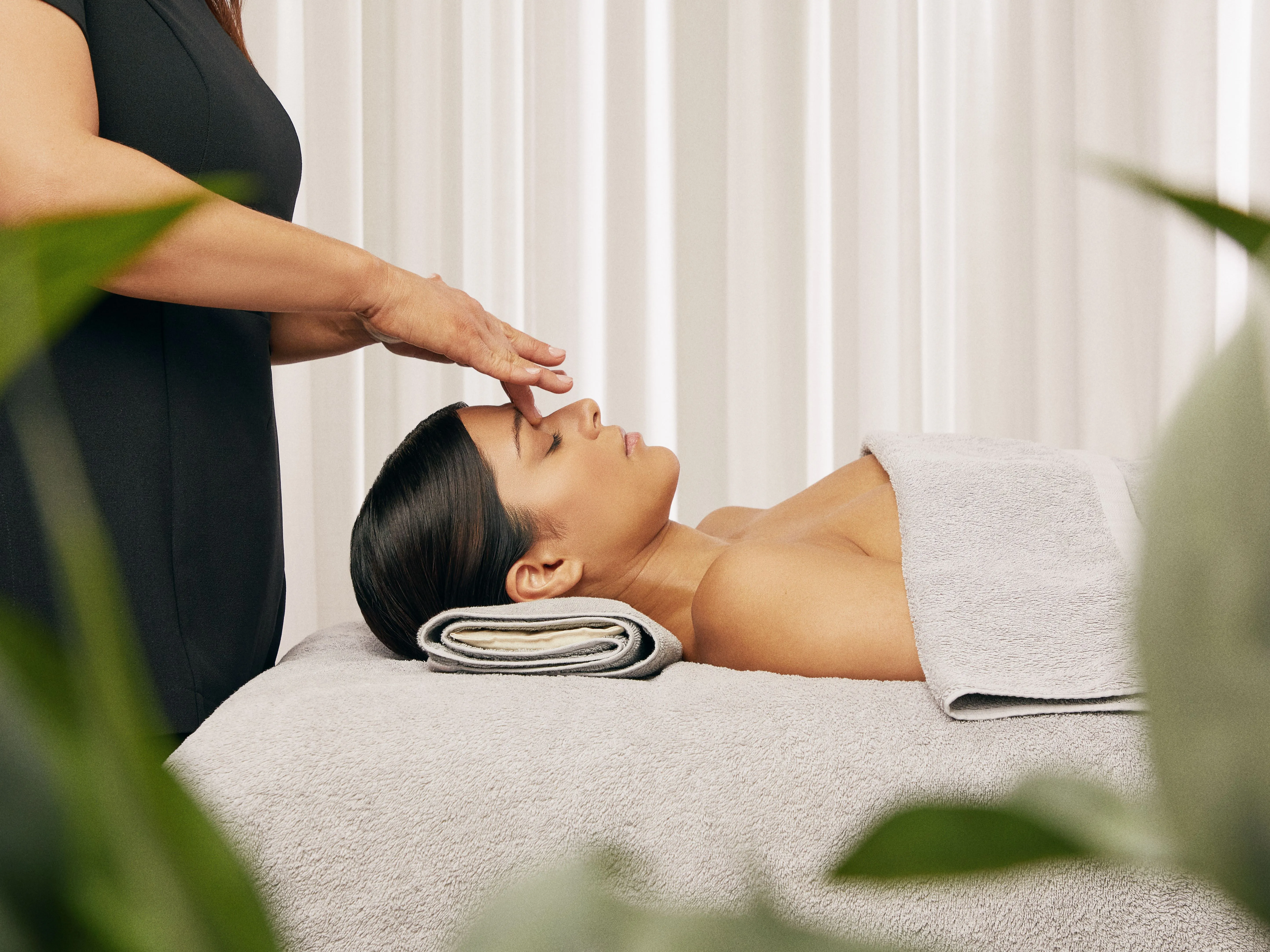 Beautician performing a relaxing facial treatment on a client lying on a spa bed with towels