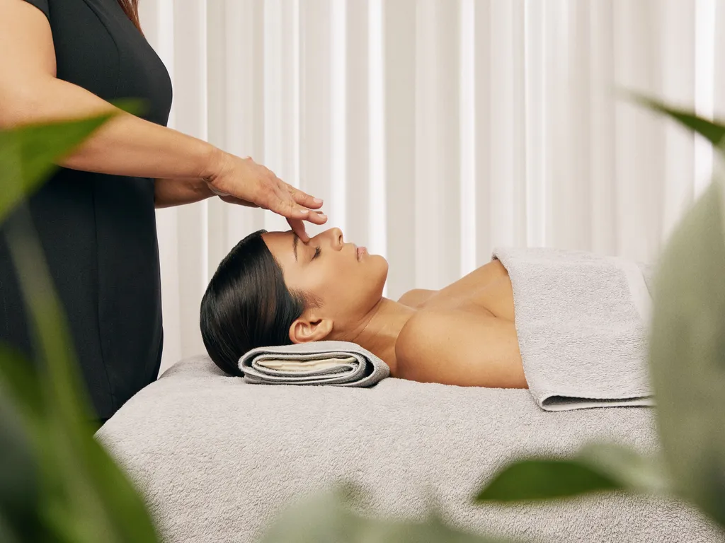 Beautician performing a relaxing facial treatment on a client lying on a spa bed with towels