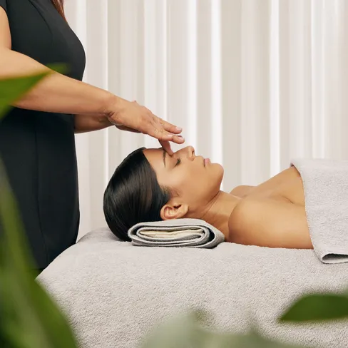 Beautician performing a relaxing facial treatment on a client lying on a spa bed with towels