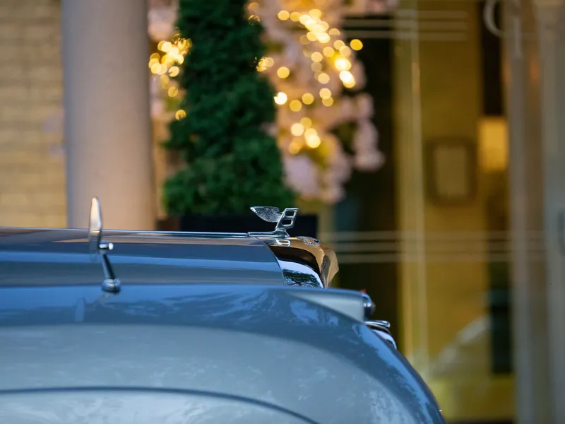 Close-up of a Bentley bonnet mascot on a grey car with warm festive lights blurred in the background
