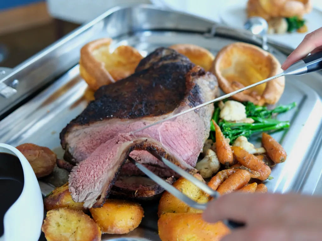 Carving roast beef with Yorkshire puddings, roast potatoes and vegetables on a serving tray