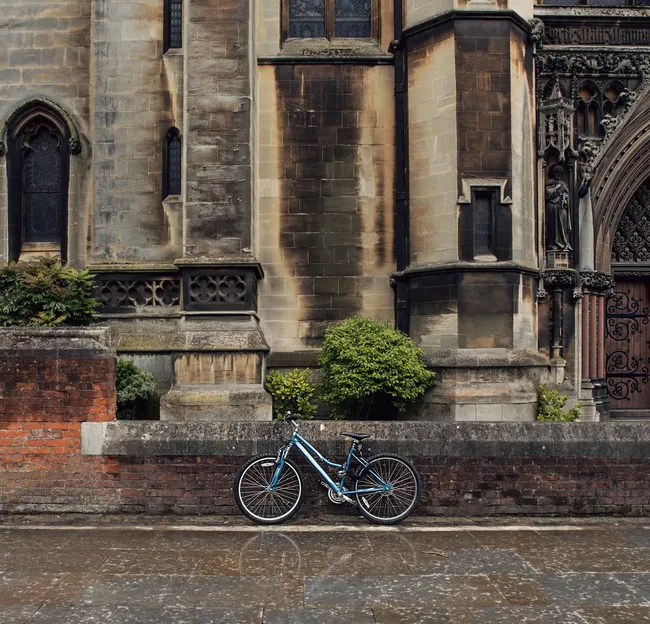 Blue bicycle parked against a brick wall in front of an old stone church with arched windows and an ornate wooden doorway.