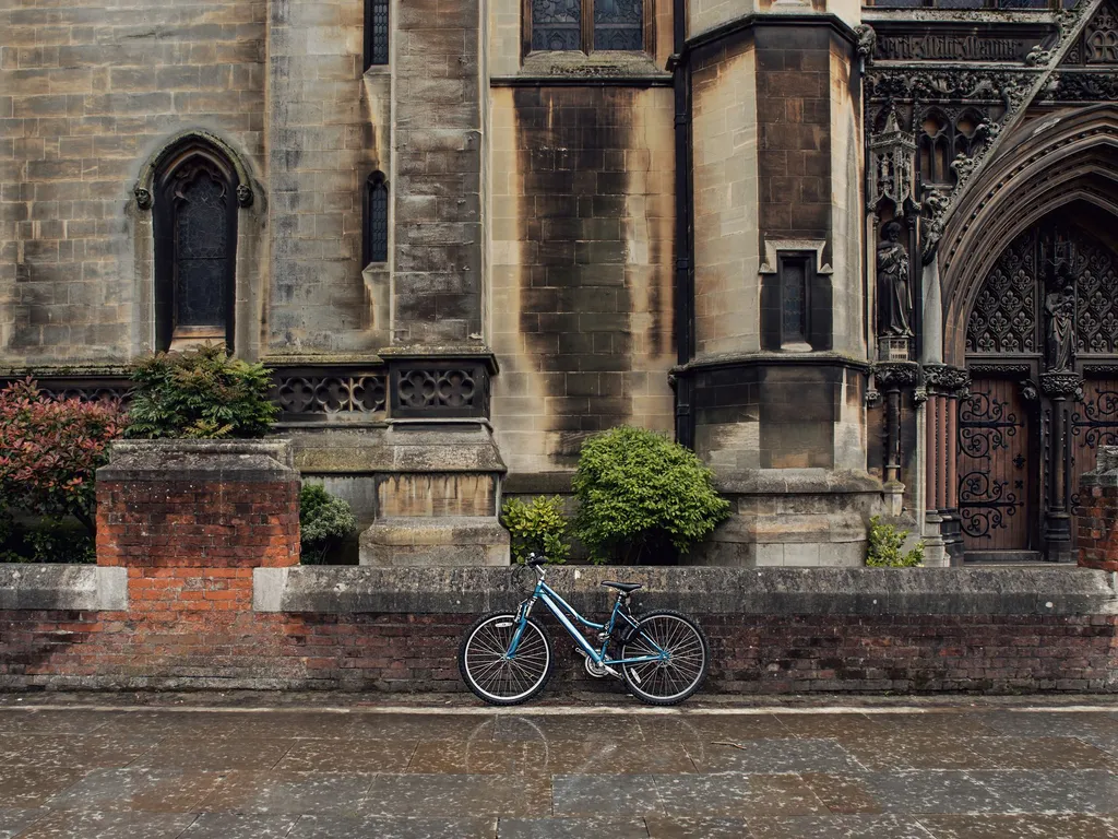 Blue bicycle parked against a brick wall in front of an old stone church with arched windows and an ornate wooden doorway.