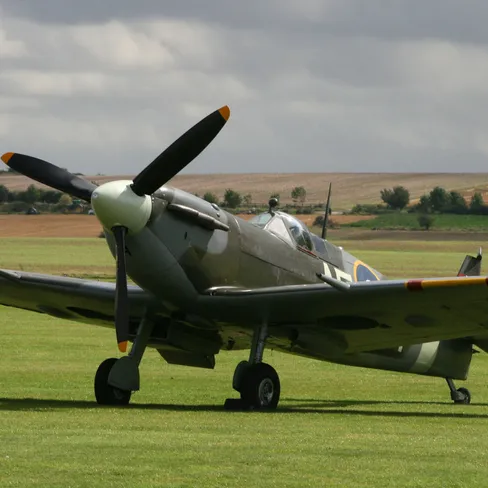 Supermarine Spitfire on the grass at Imperial War Museum Duxford, with its propeller and camouflaged wings under a cloudy sky.